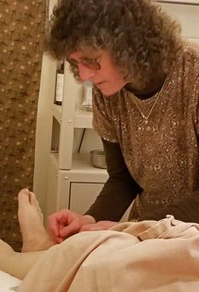 Photograph of Laurie with intently focused expression providing acupuncture treatment on a patients' lower leg